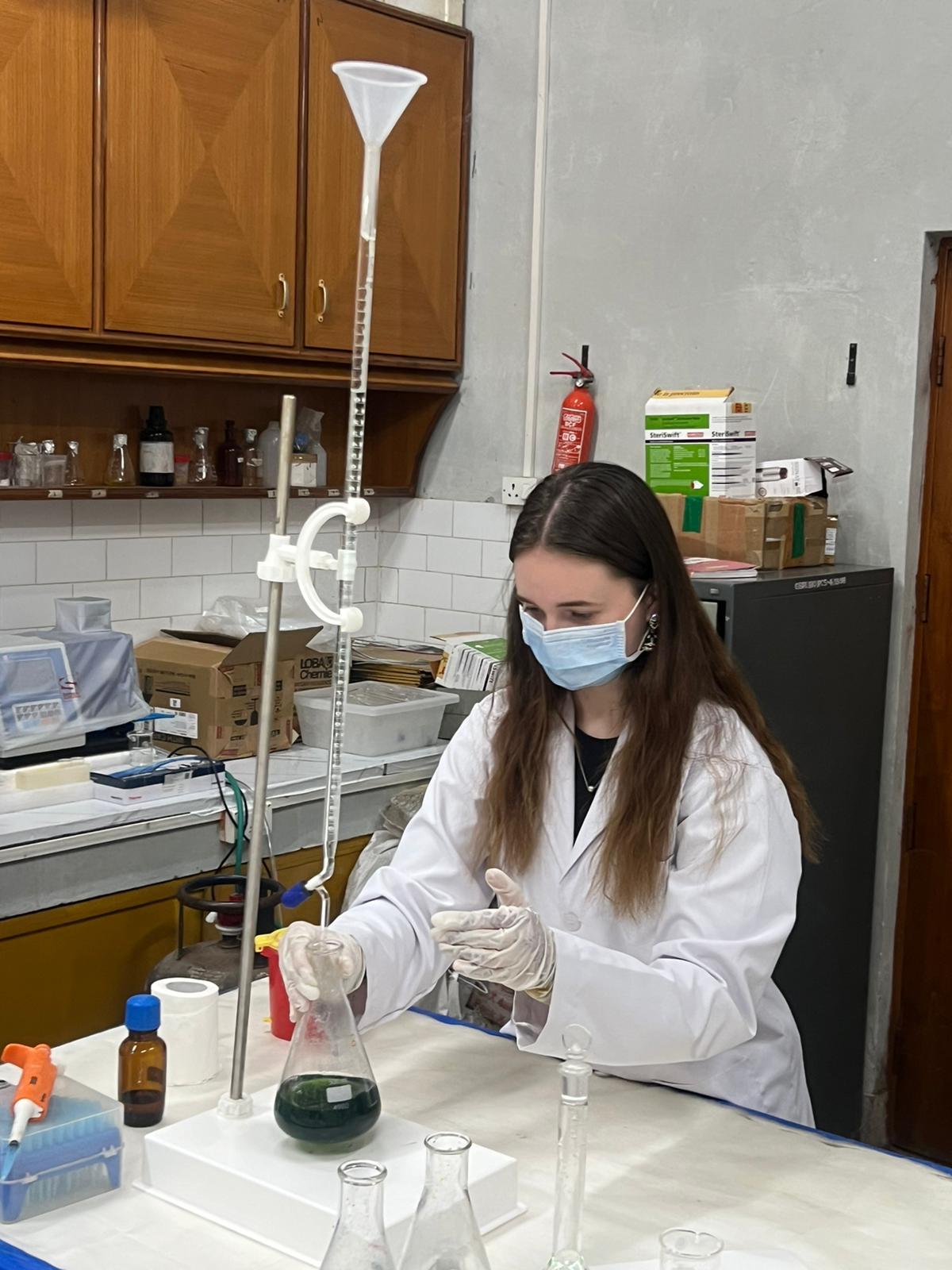 A young person with long dark hair in a white coat doing experiments in a laboratory