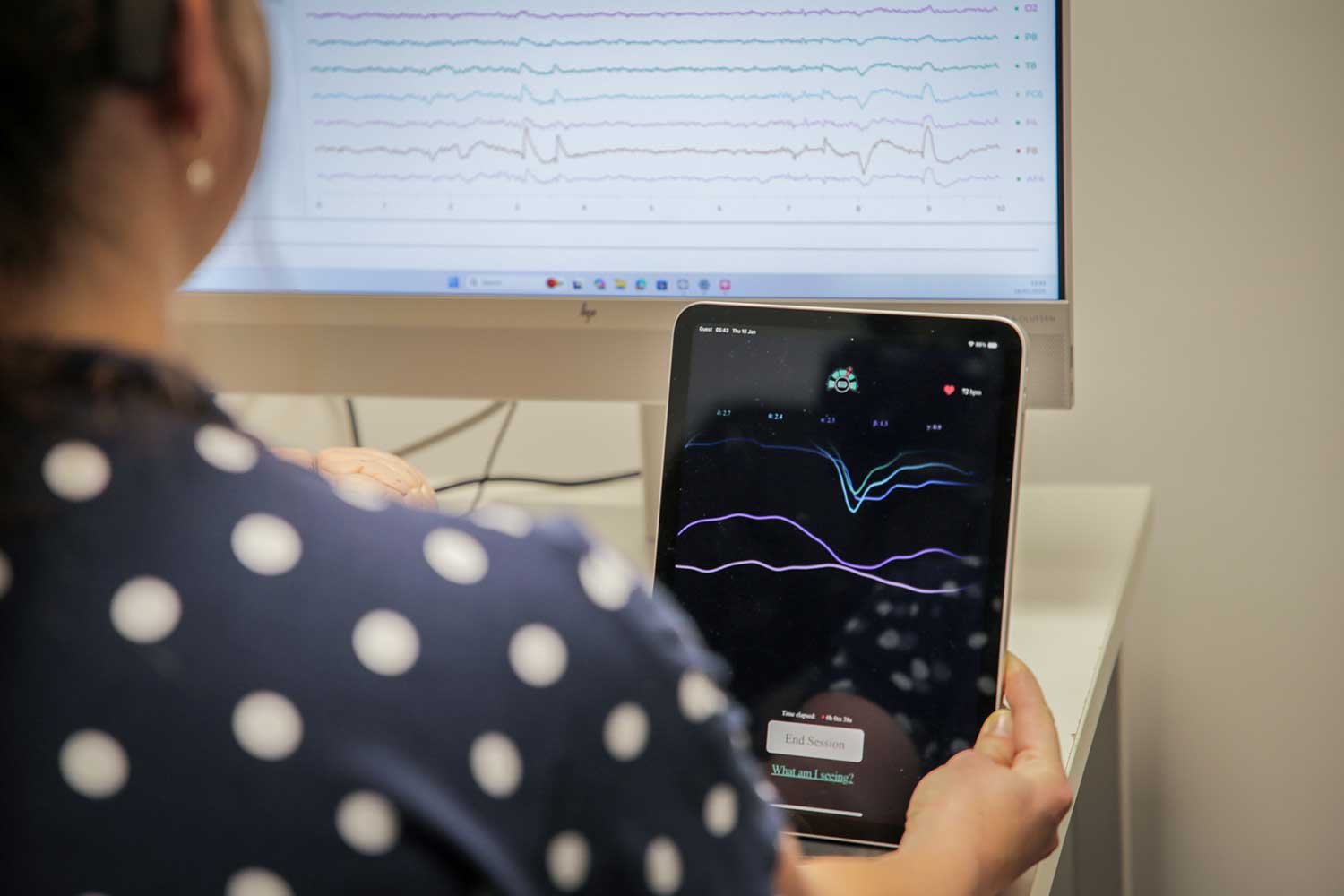 A student sitting in front a monitor uses an iPad as part of a psychology experiement