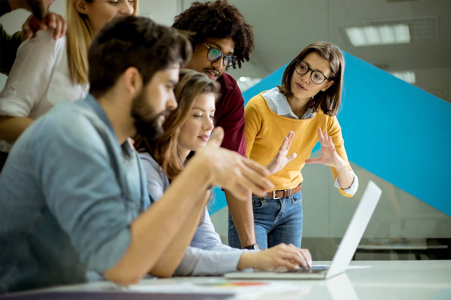 Group of diverse young people collaborating around a laptop in an office