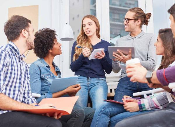 Photo of diverse group of young people discussing with pens and pads