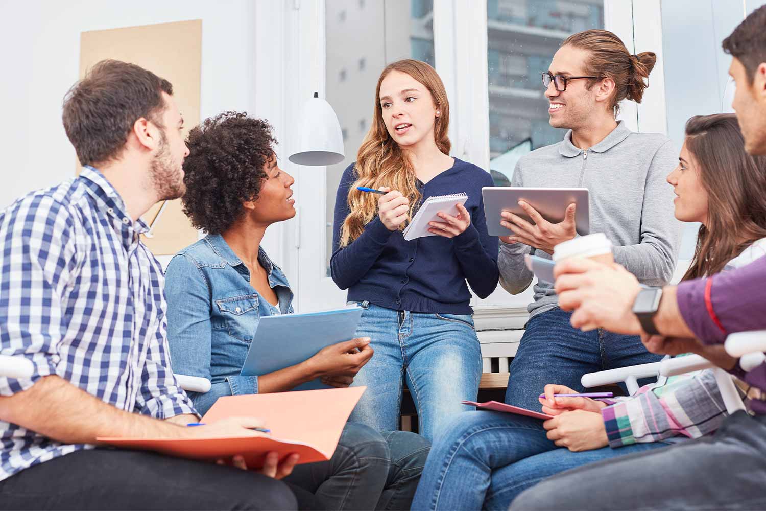 Photo of diverse group of young people discussing with pens and pads