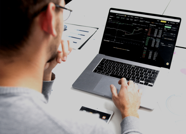 a man sits at his desk typing on his laptop. The laptop is showing a chart of data.