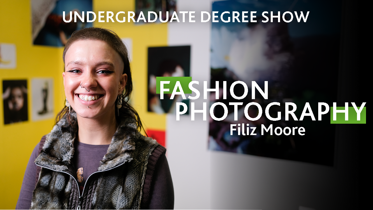 A person with bold eyeliner and several piercings smiles at the camera