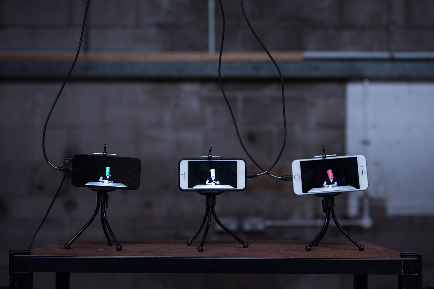 A dark room with three smartphones on mini tripods with images on the screens sat on the table.
