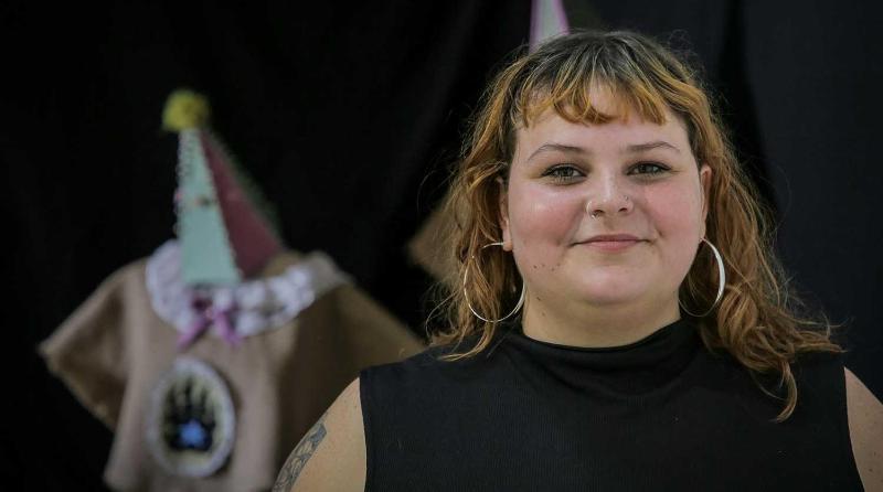 A student with shoulder-length hair stands in front of items from their degree show exhibition