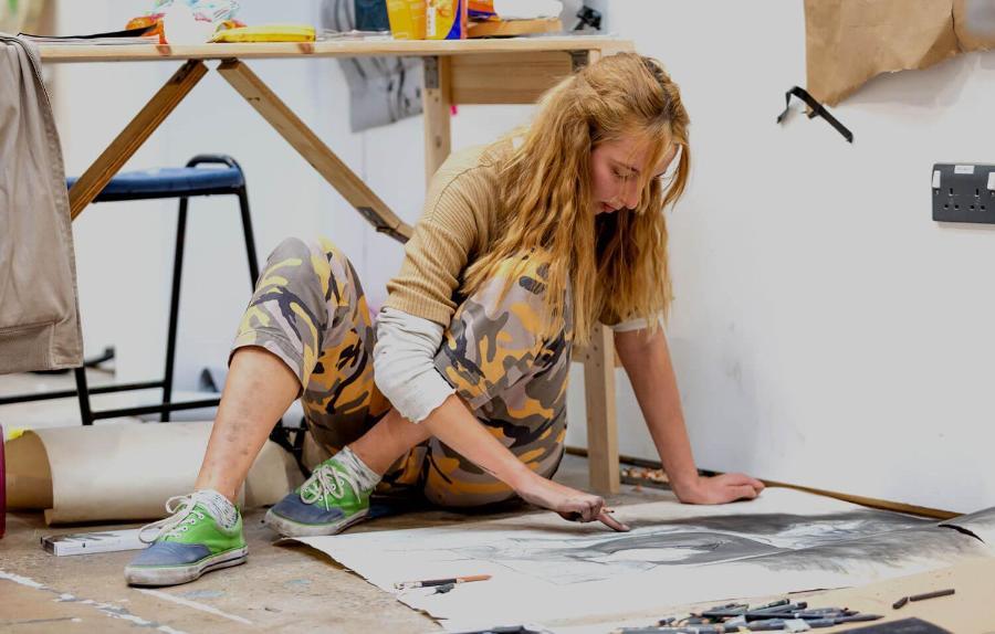 Student sitting on the floor, using pencil to create a large sketch