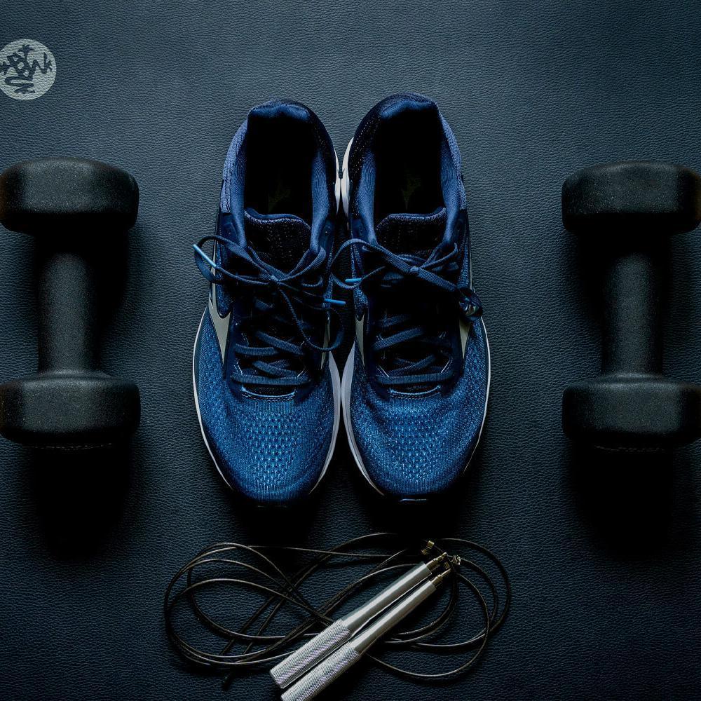 A pair of running shoes, some dumbbells and a skipping rope on a gym mat