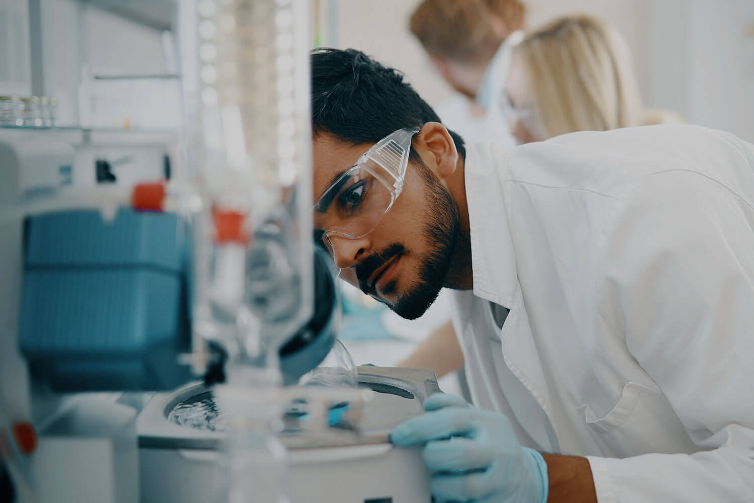 A student wearing safety goggles leans over a piece of laboratory equipment