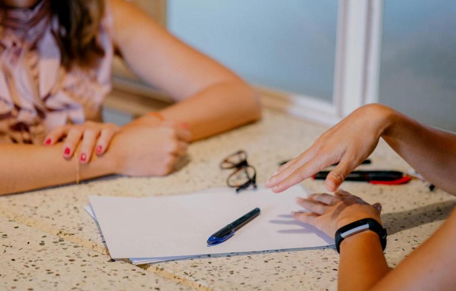 Two women in conversation at table with stationery on it