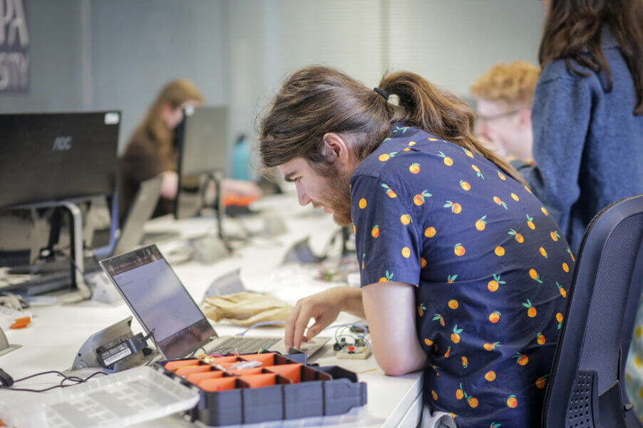 A student wearing a blue shirt with orange fruits on it working at a laptop.