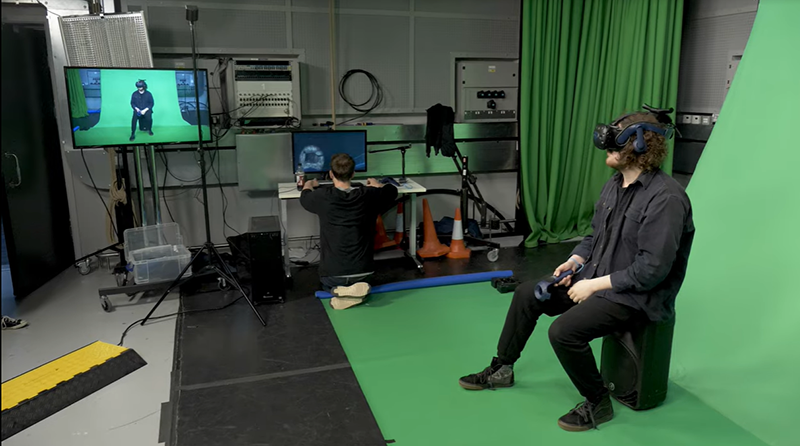 A person wearing a VR headset and sitting in front of a green screen.