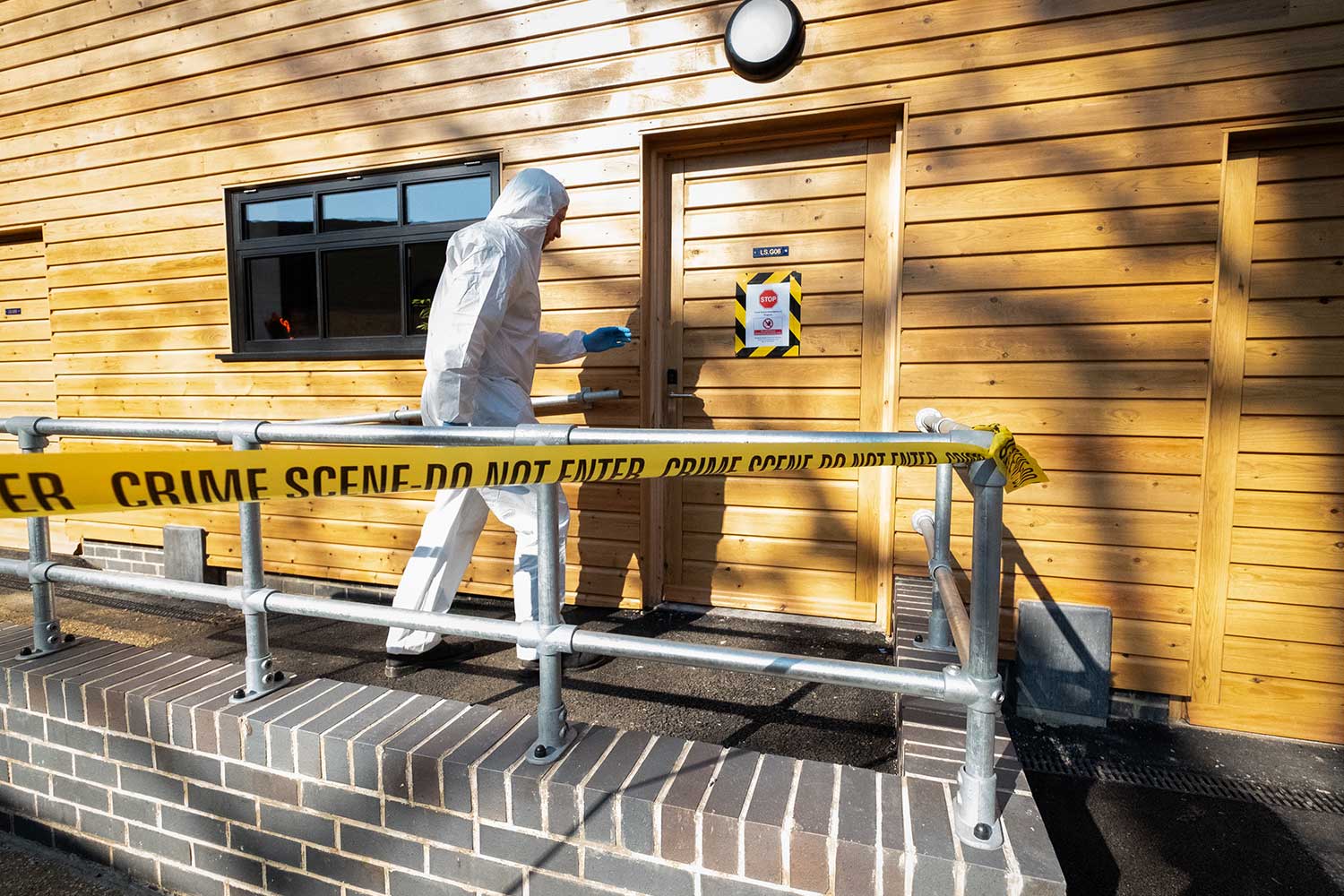 A person wearing personal protective equipment walks past crime scene tape