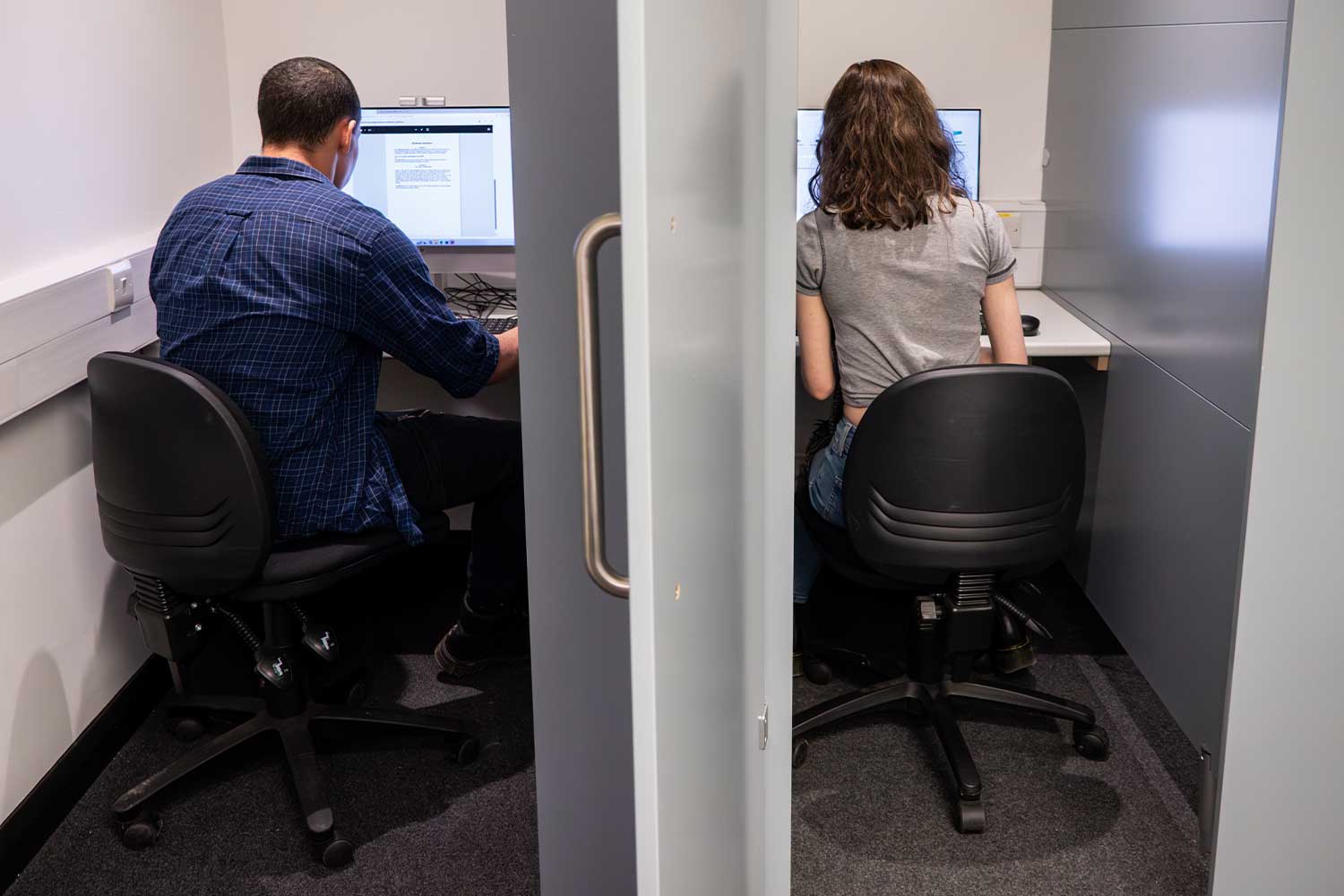 Two students sit at computers in separate rooms