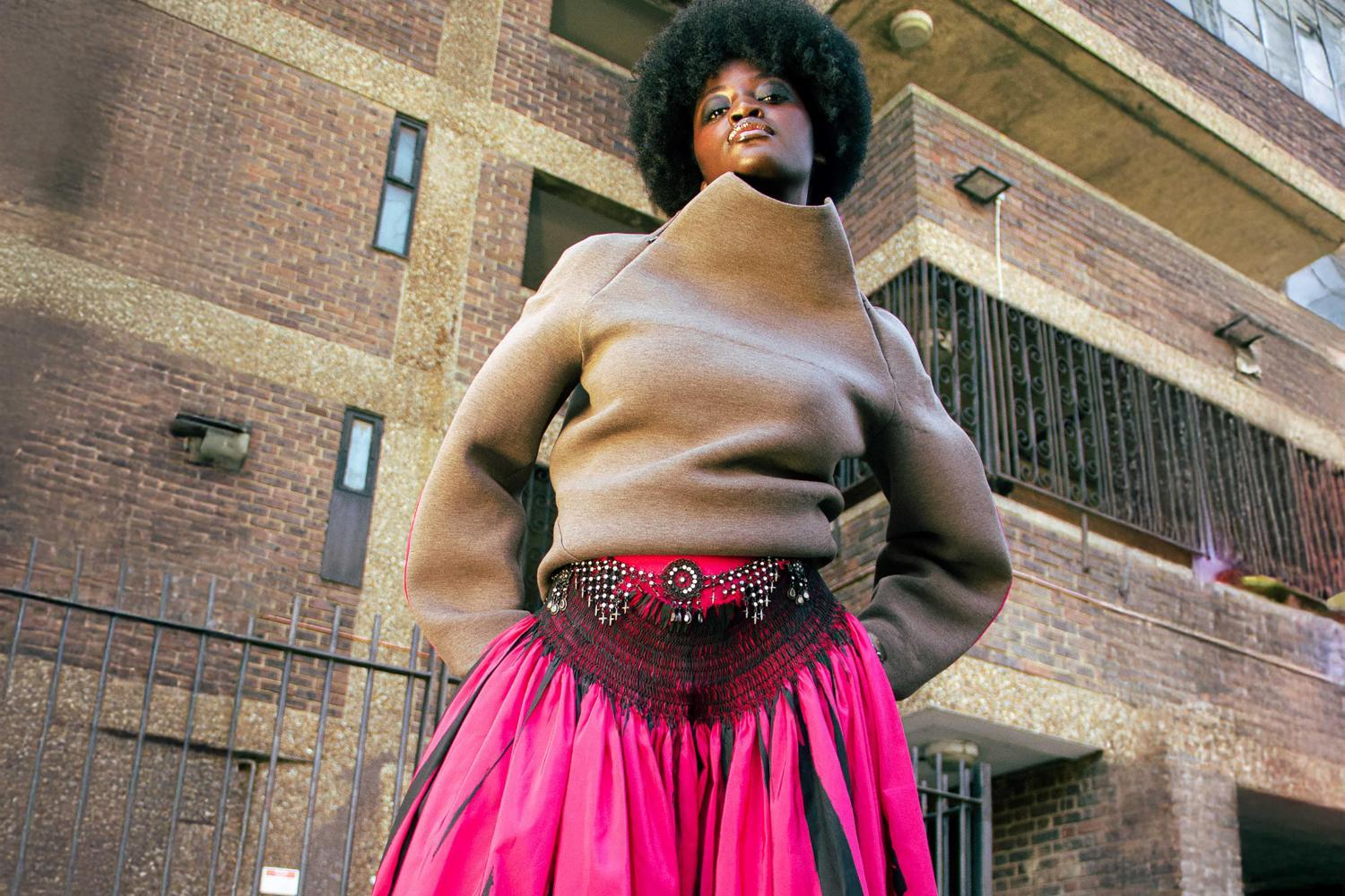  A model wearing a voluminous fuchsia pink skirt and light brown knitted long-sleeved top