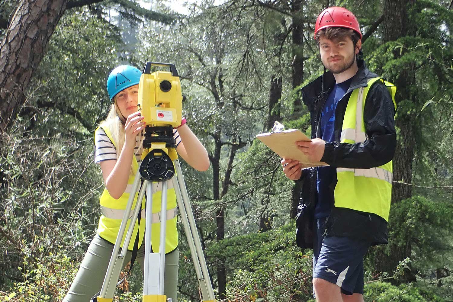 Two students operate equipment in a woodland area