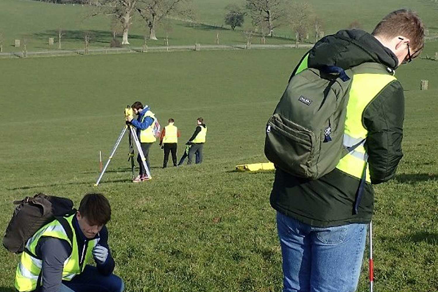 A group of students wear high vis jackets in a field
