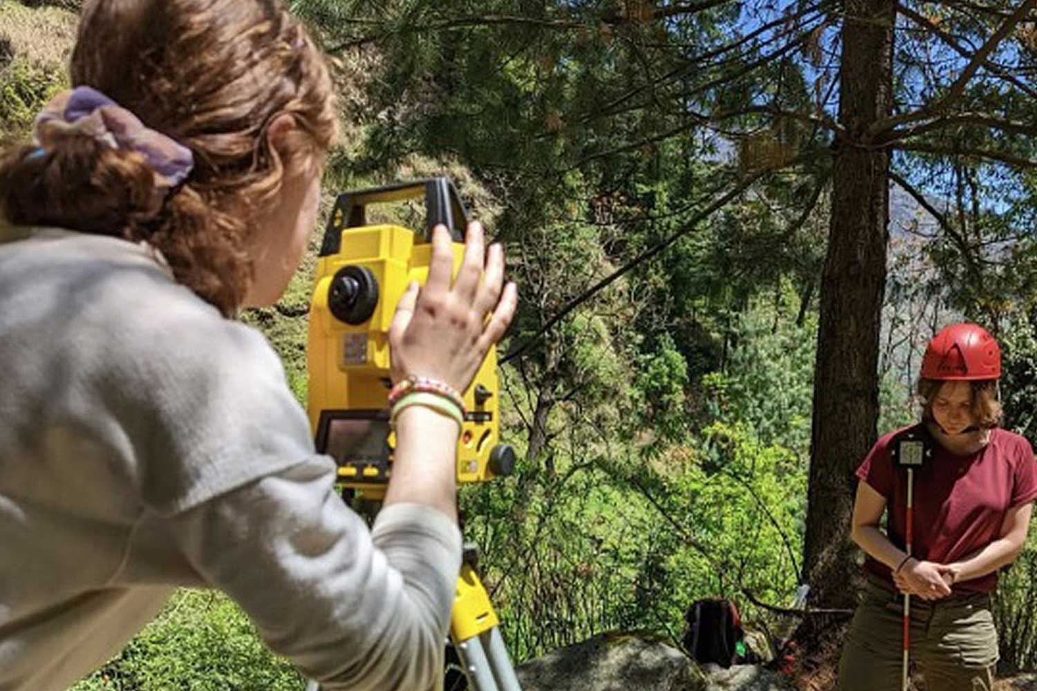 Two students operate equipment in a woodland area