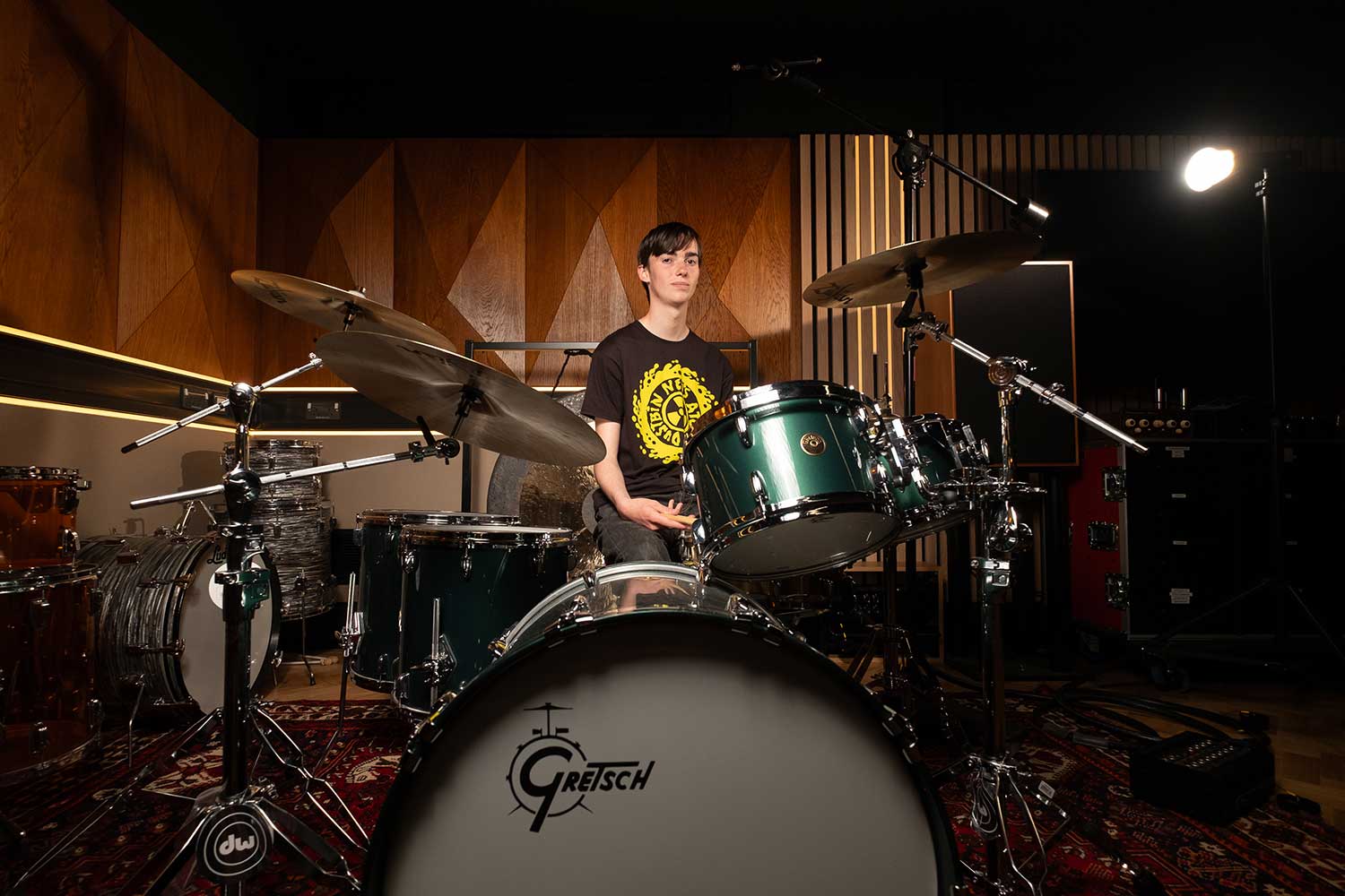 A student sits behind a drumkit in a music studio