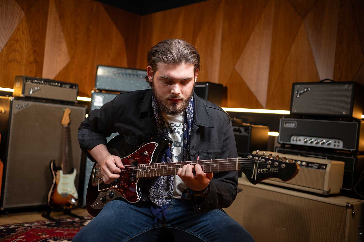 A music student leans over their guitar in a recording studio