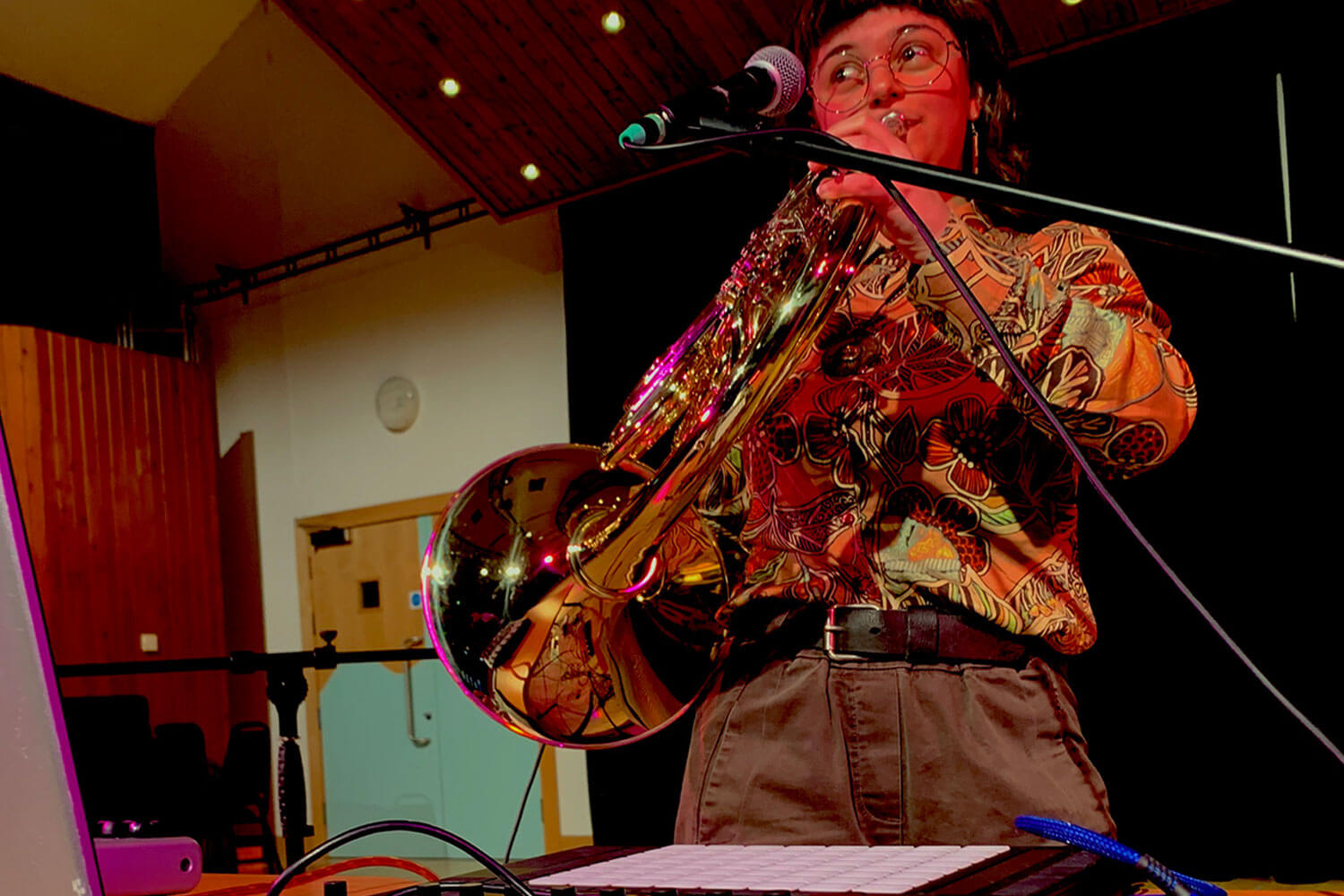Student plays trumpet while standing near a laptop and electronic equipment