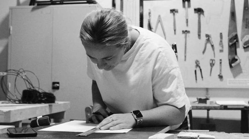 A student leans over a workbench to measure a diagram