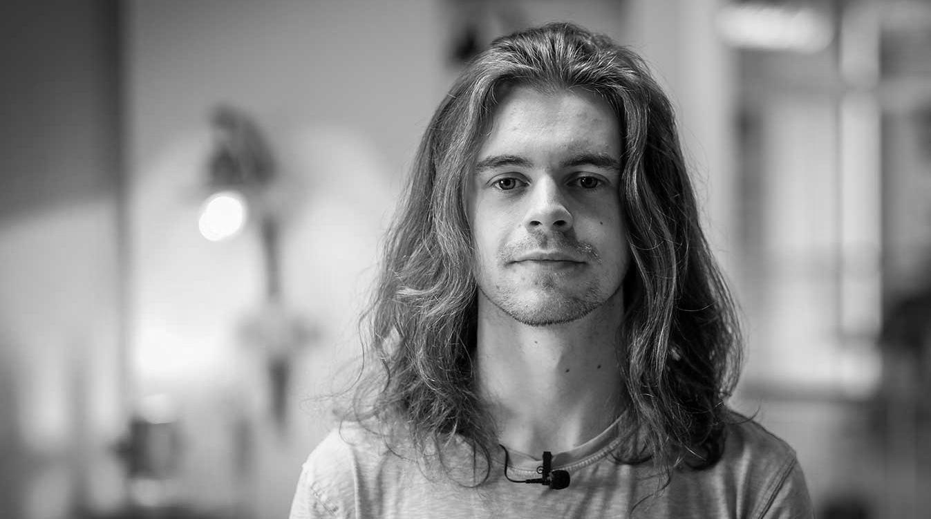 A student with shoulder-length brown hair looks into the camera lens