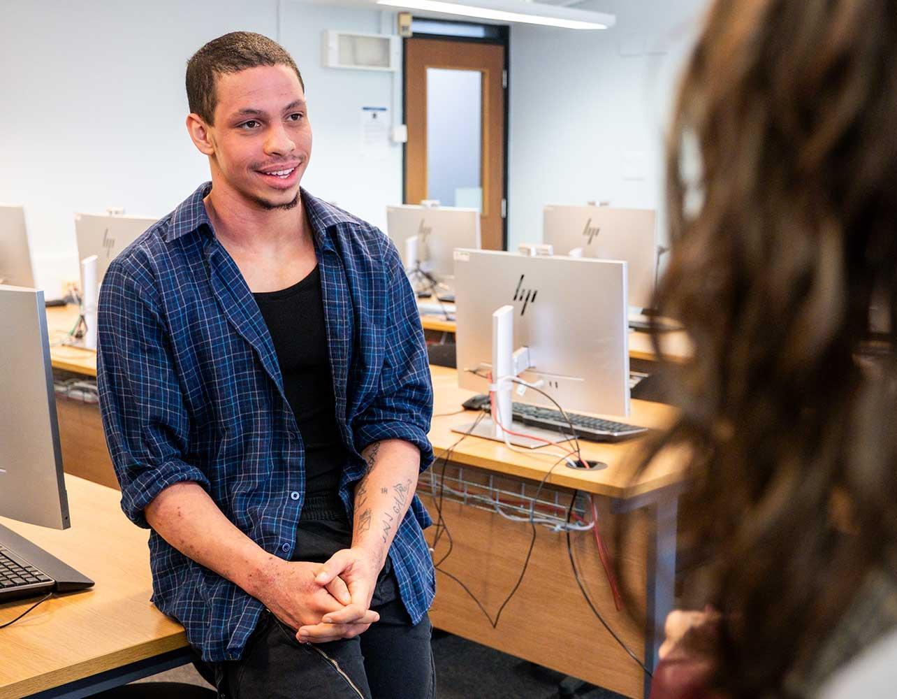 A psychology student leans on a table as they talk to other students