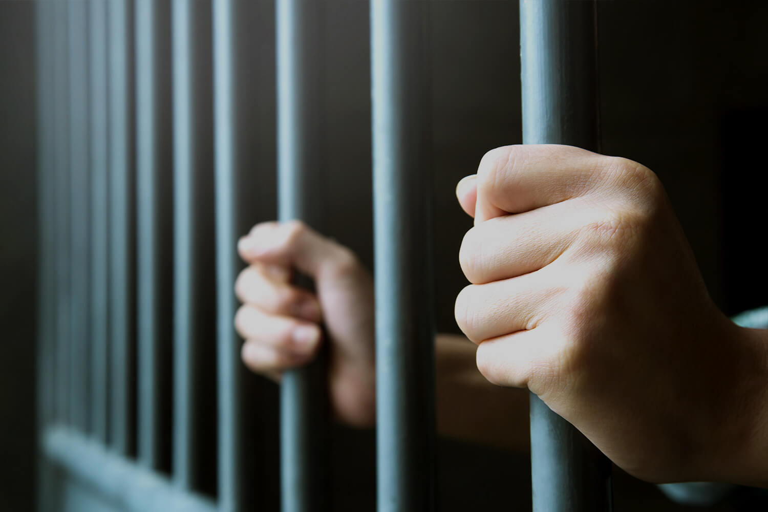 Hands around steel cage jail bars.