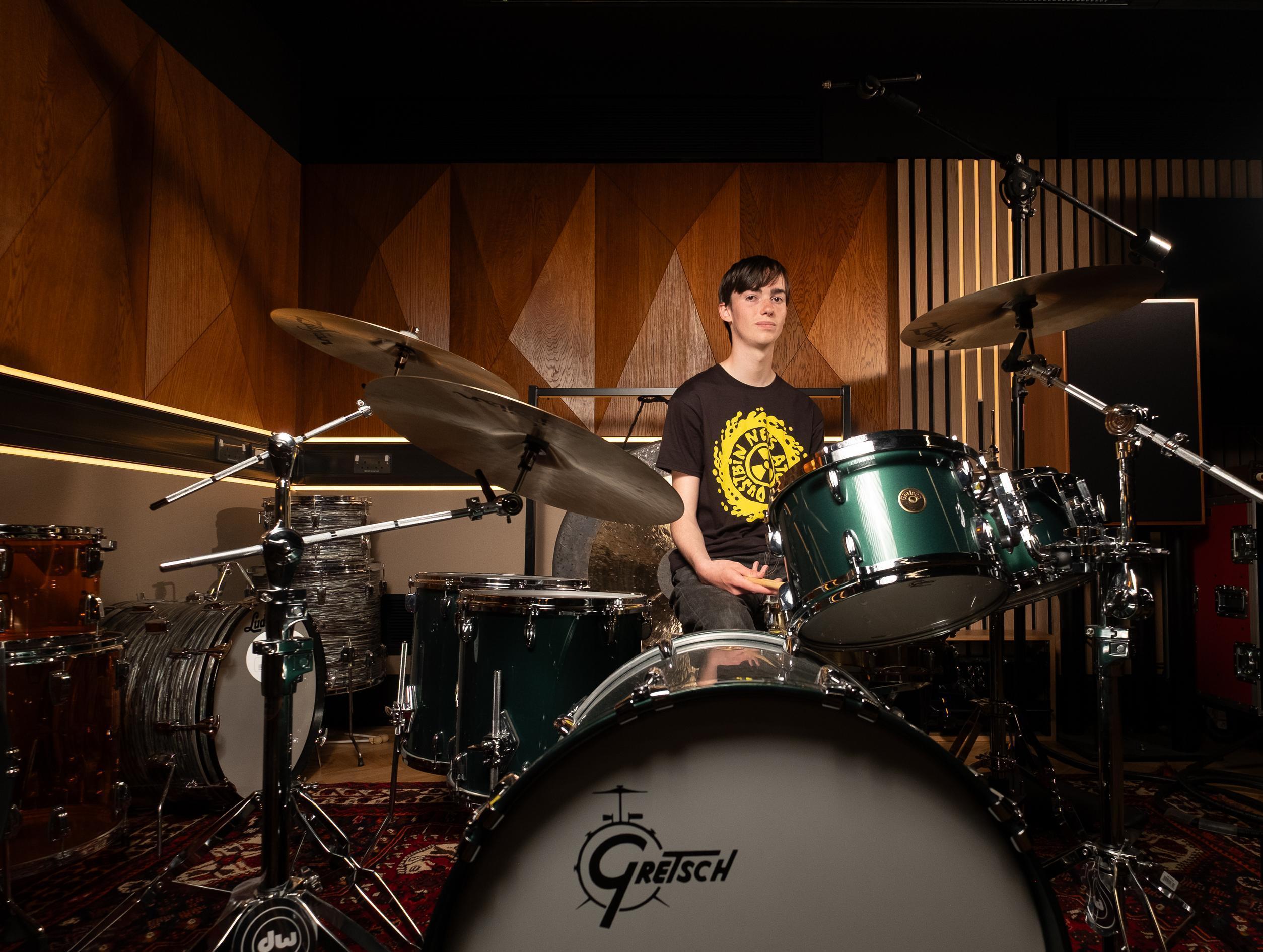 A student sits behind a drumkit in a music studio