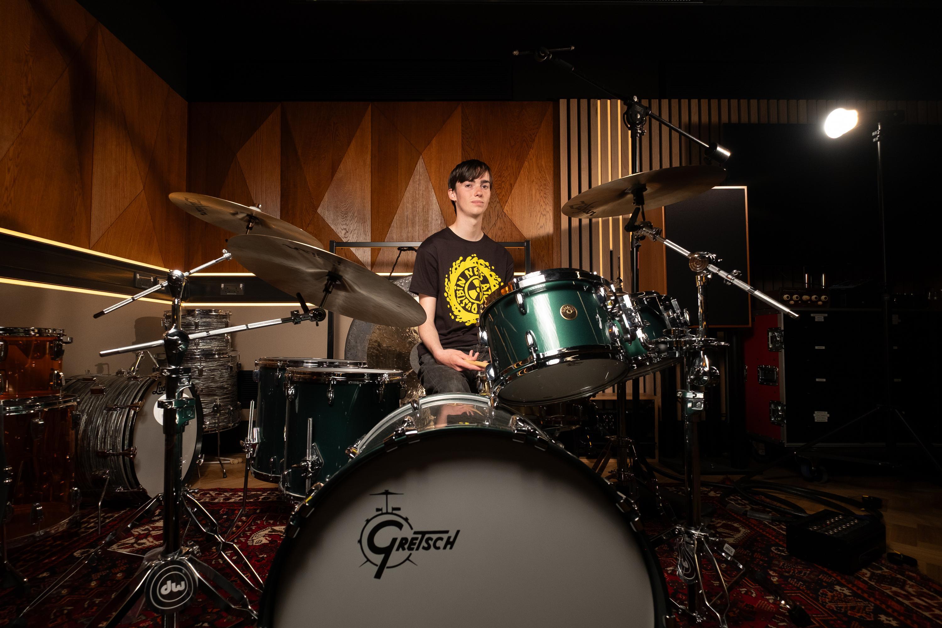 A student sits behind a drumkit in a music studio