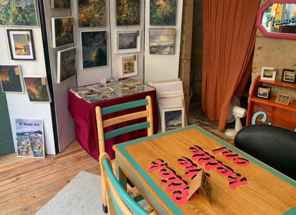 Image of a working gallery with paintings for sale on shelves and desk