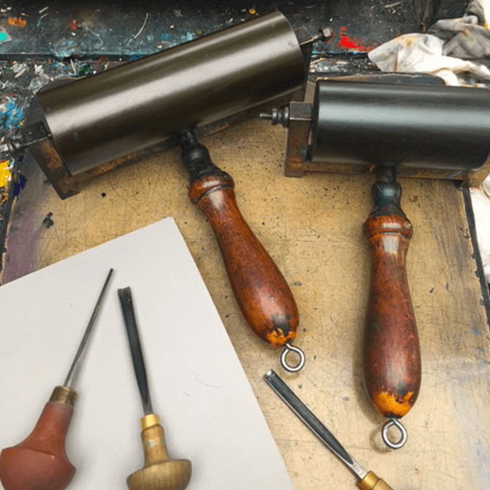 A selection of chisels and ink rollers laid on top of a lino block