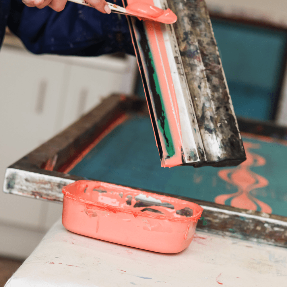 A hand scraping ink off of a squeegee