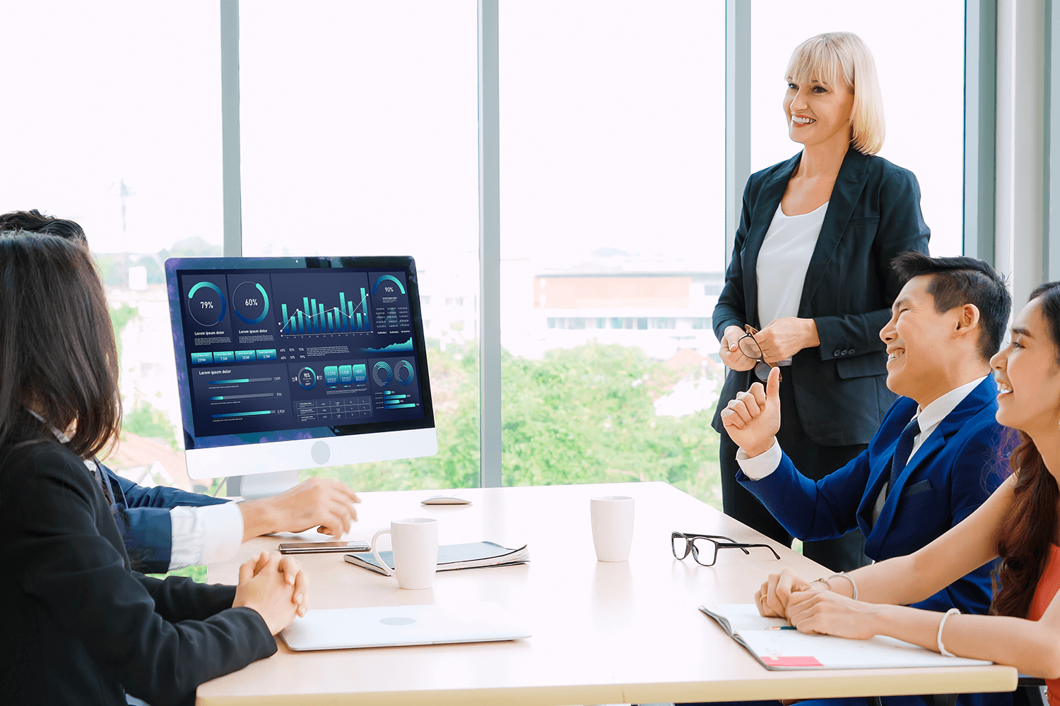 A group of coworkers sit around a table listening to a colleague present a data dashboard