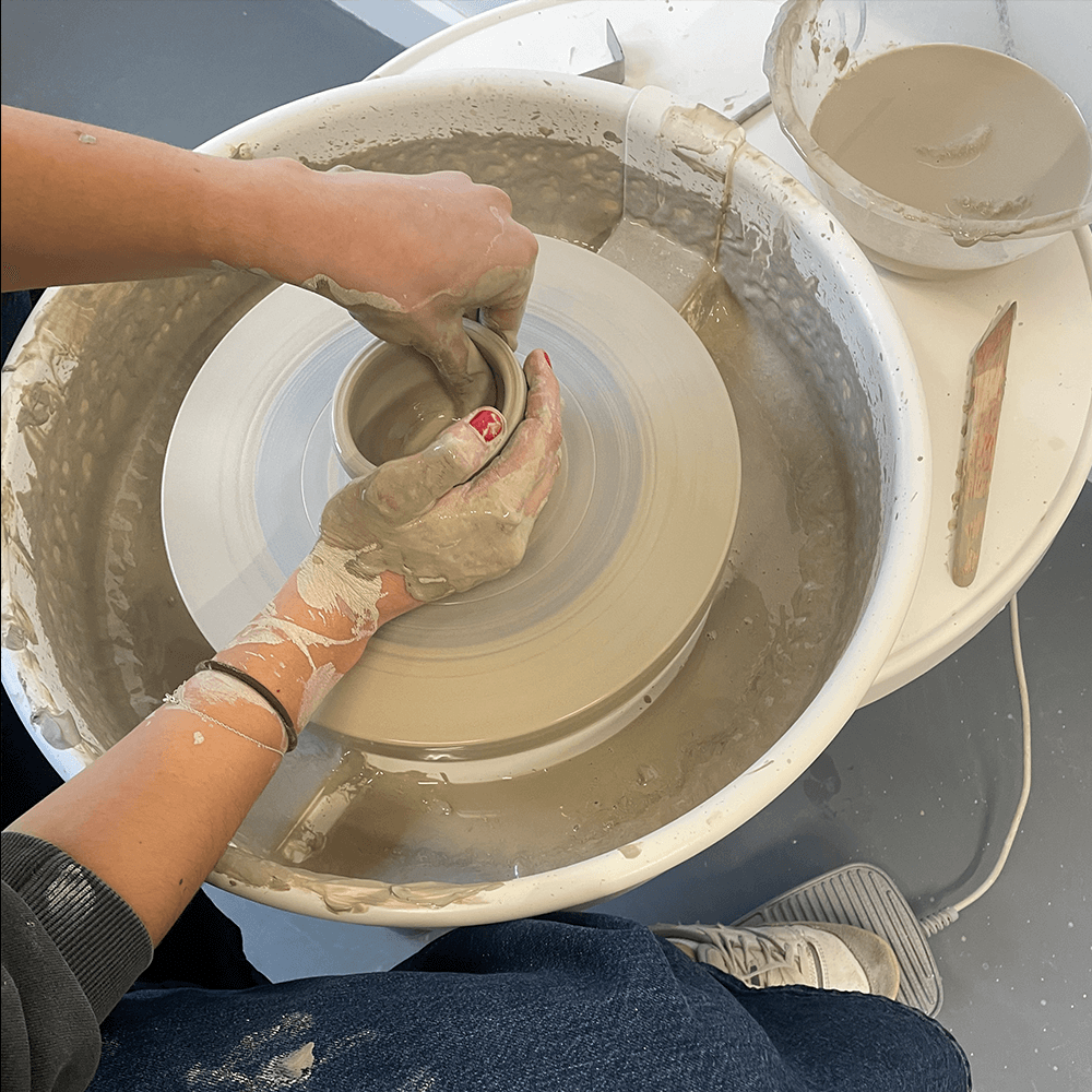 A pair of hands pinching a pot on a pottery wheel.