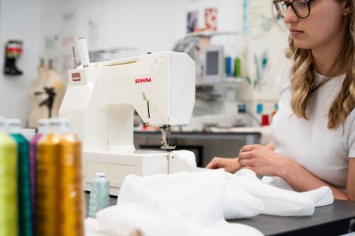 A female student sat at a sewing machine sewing white fabric