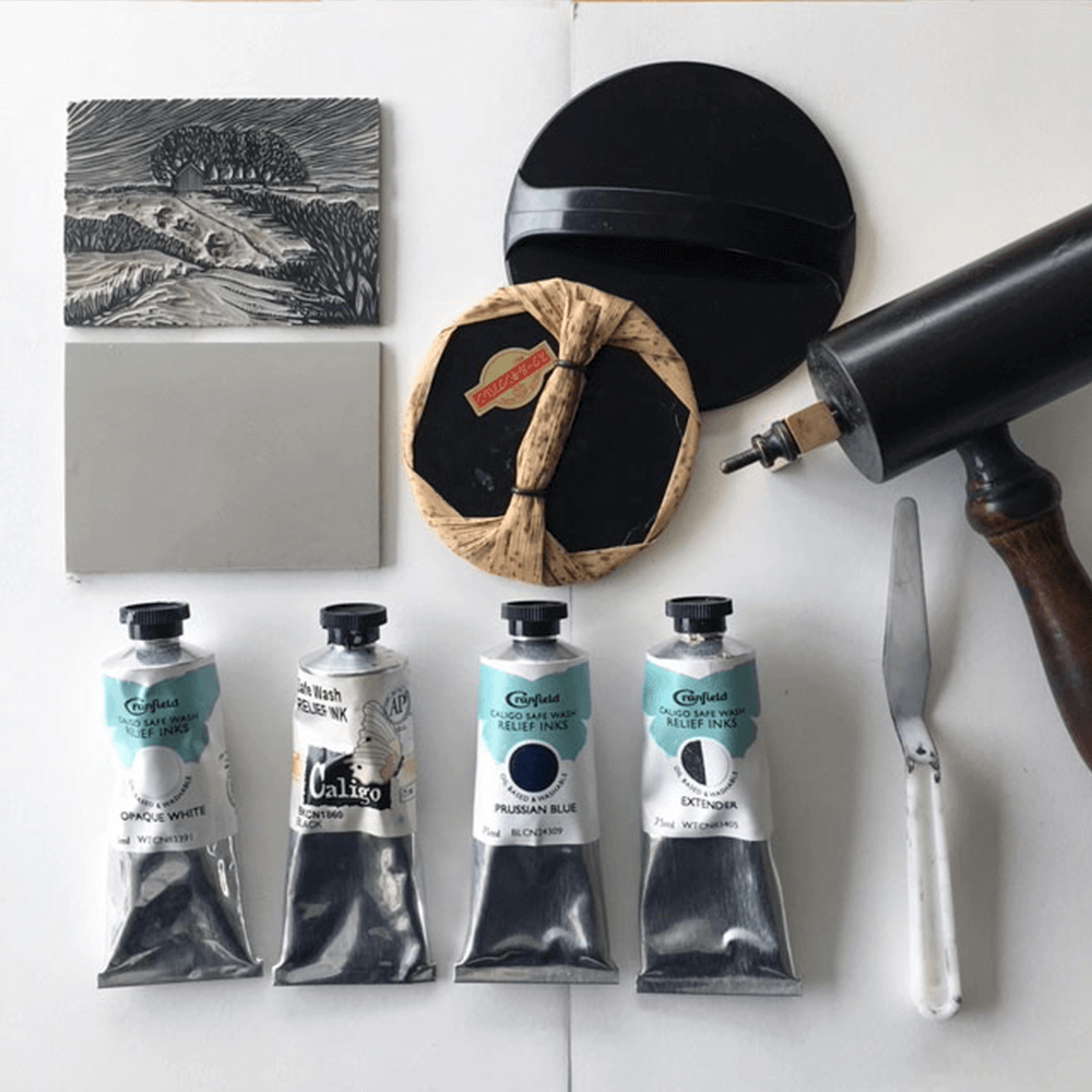 A flat lay of a lino block, inks and linocutting tools