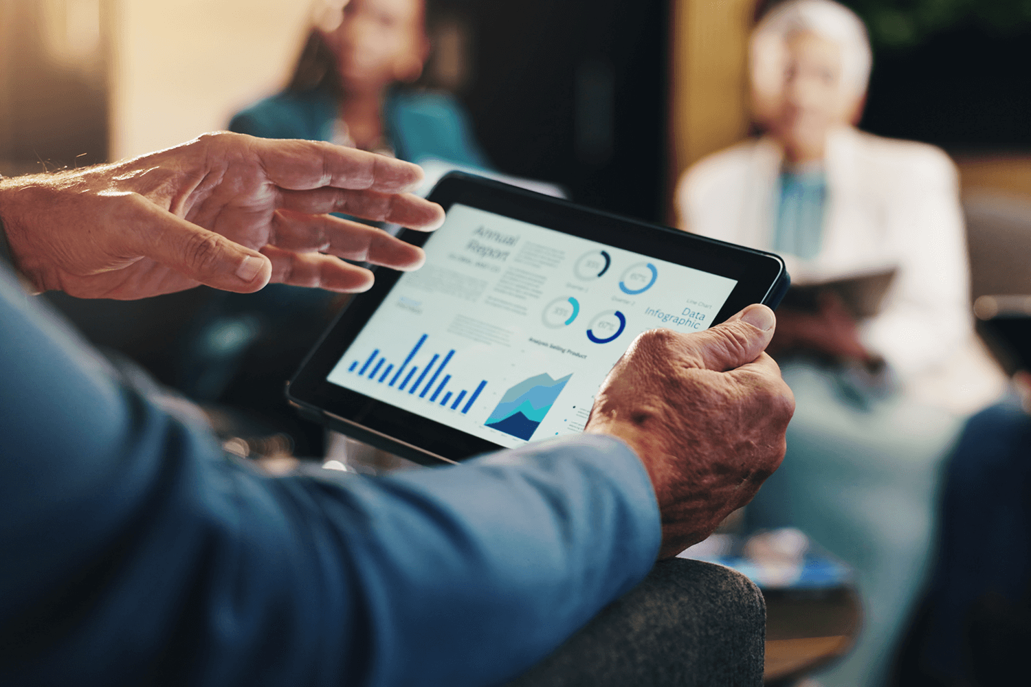 A man holds a tablet showing a data dashboard and presents to his coworkers
