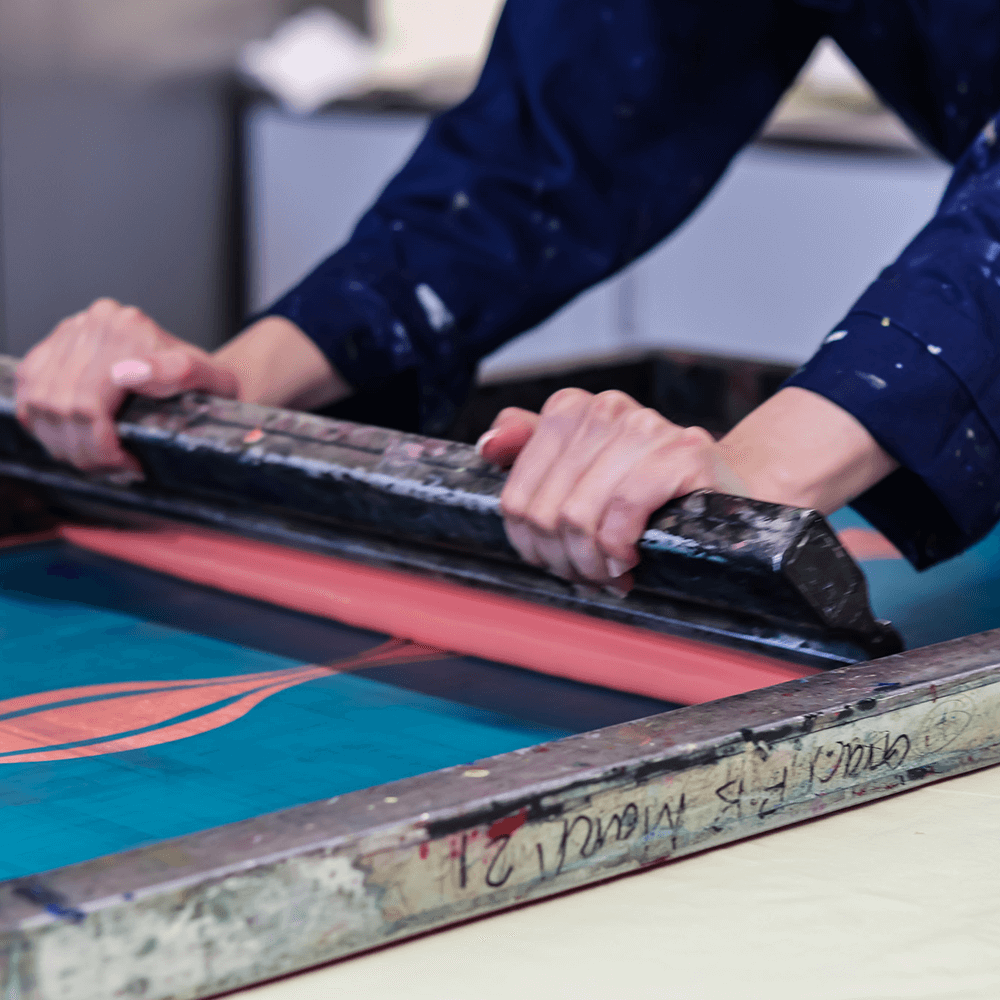 A student pulling a screenprinting squeegee across a silk screen