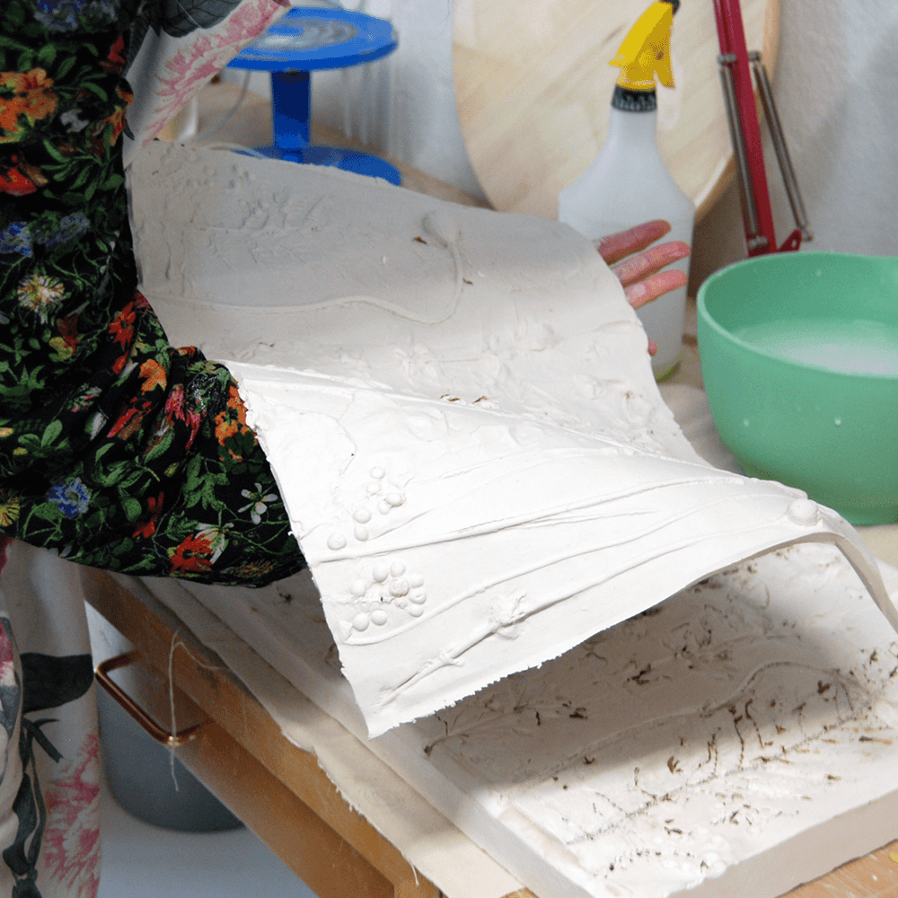 A person holds a sheet of clay with sculpted plants inlaid on top