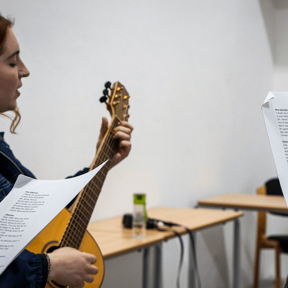Two students stood singing, one is playing a guitar