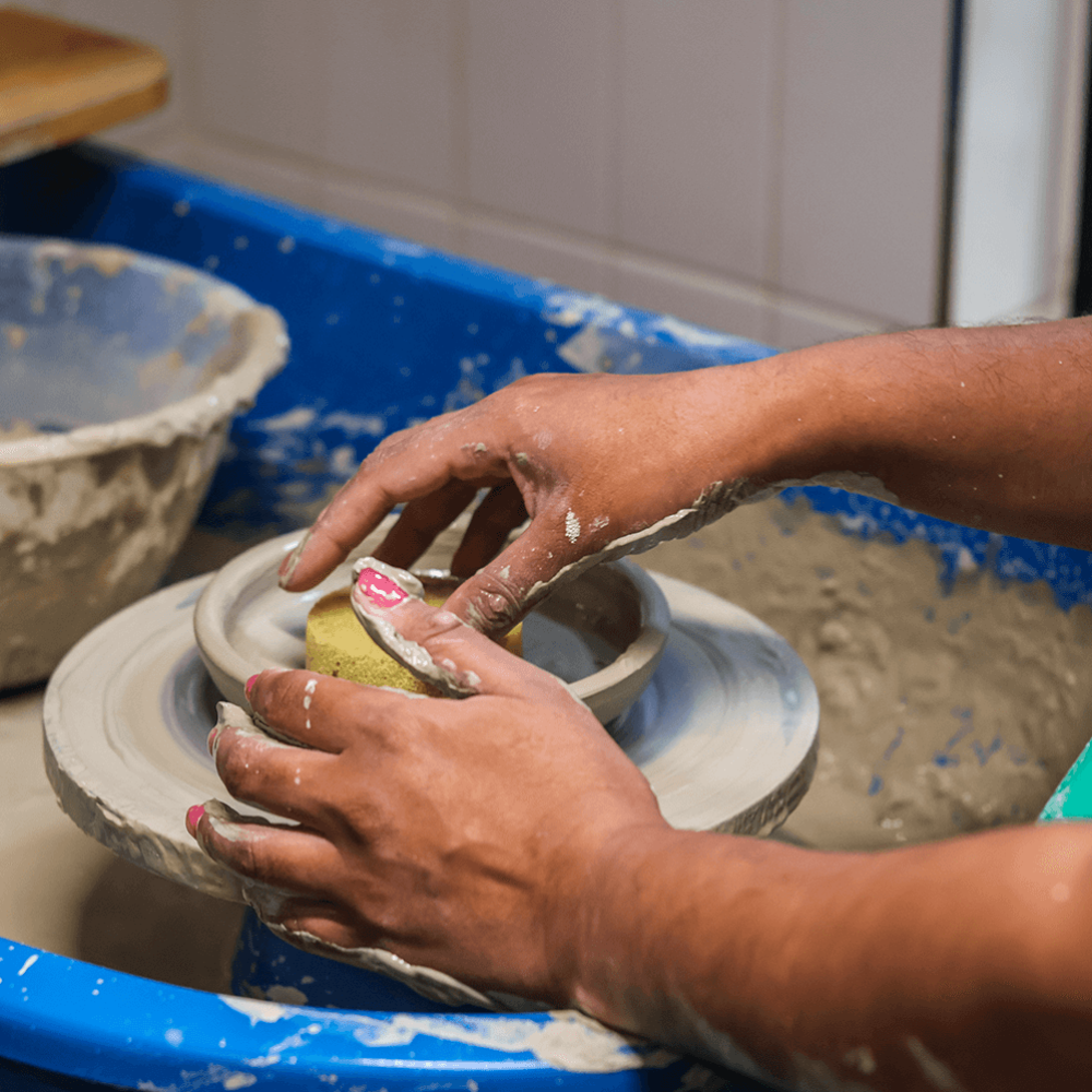 A person sat at a pottery wheel smoothing out a bowl with a sponge
