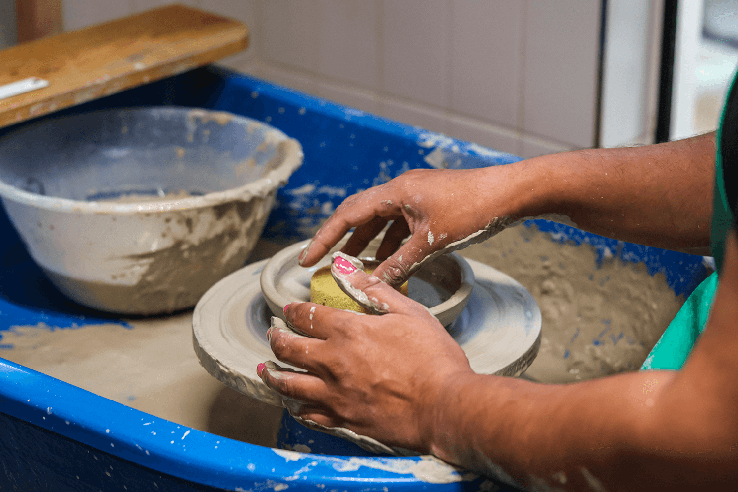 A person sat at a pottery wheel smoothing out a bowl with a sponge
