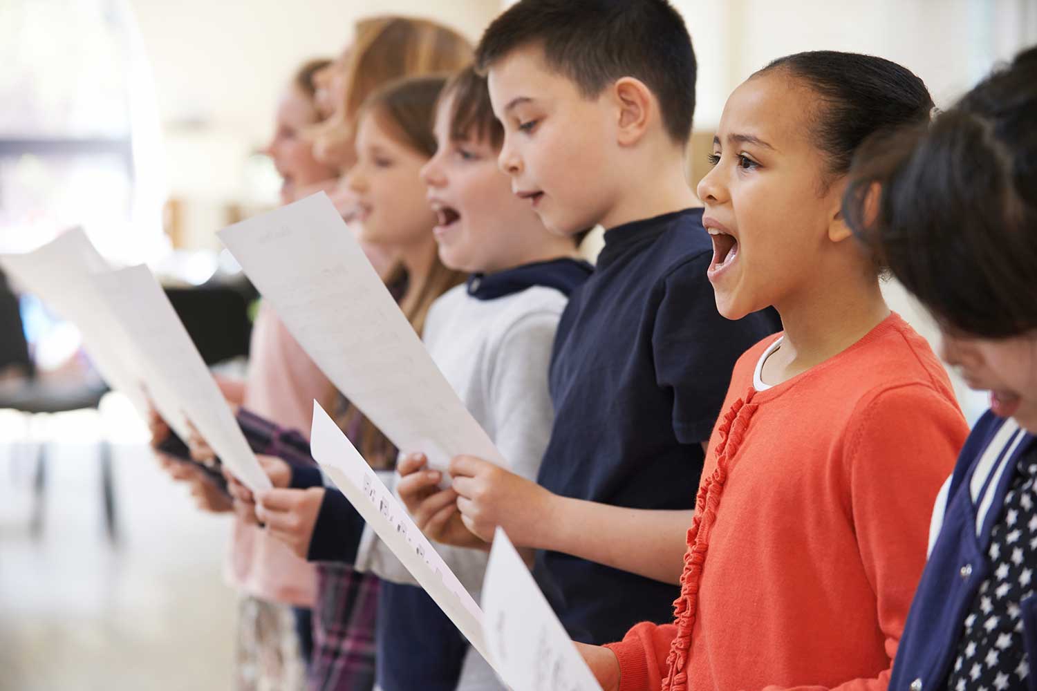 A row of children singing and holding sheets of paper