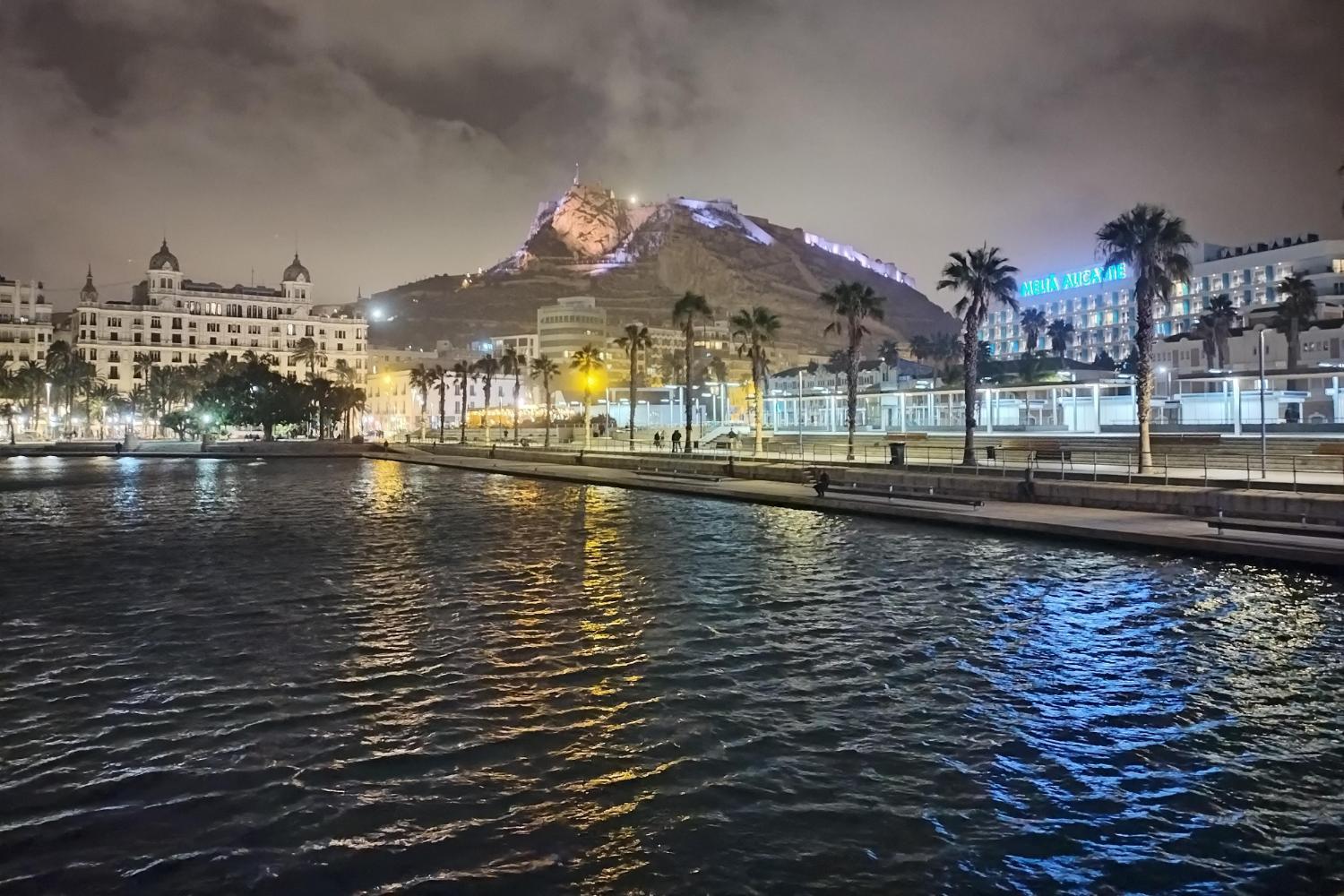 A waterfront town in front of a mountain light by colourful lights at night