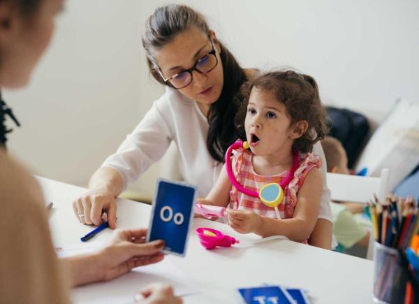 A speech therapist sits opposite a mother and child practising phonetics