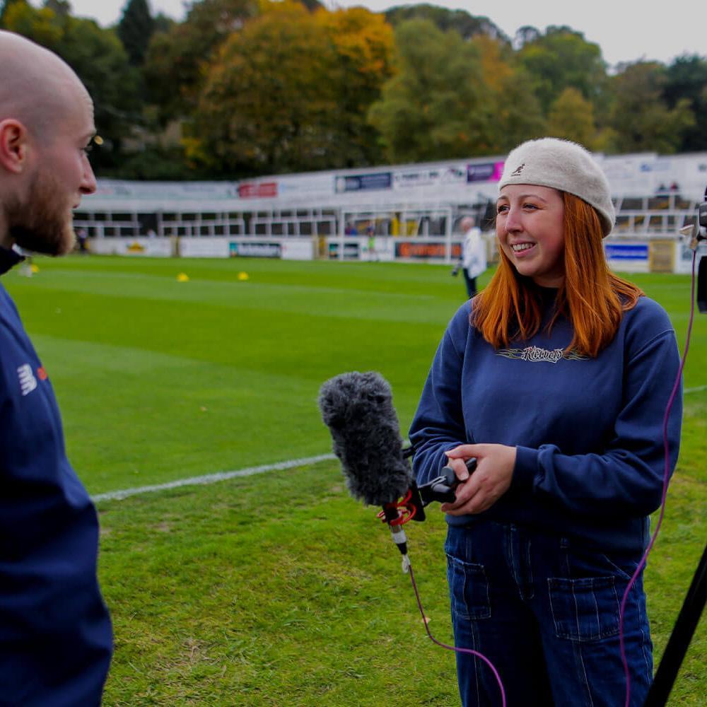 Student with mic talking with sports professional on a pitch