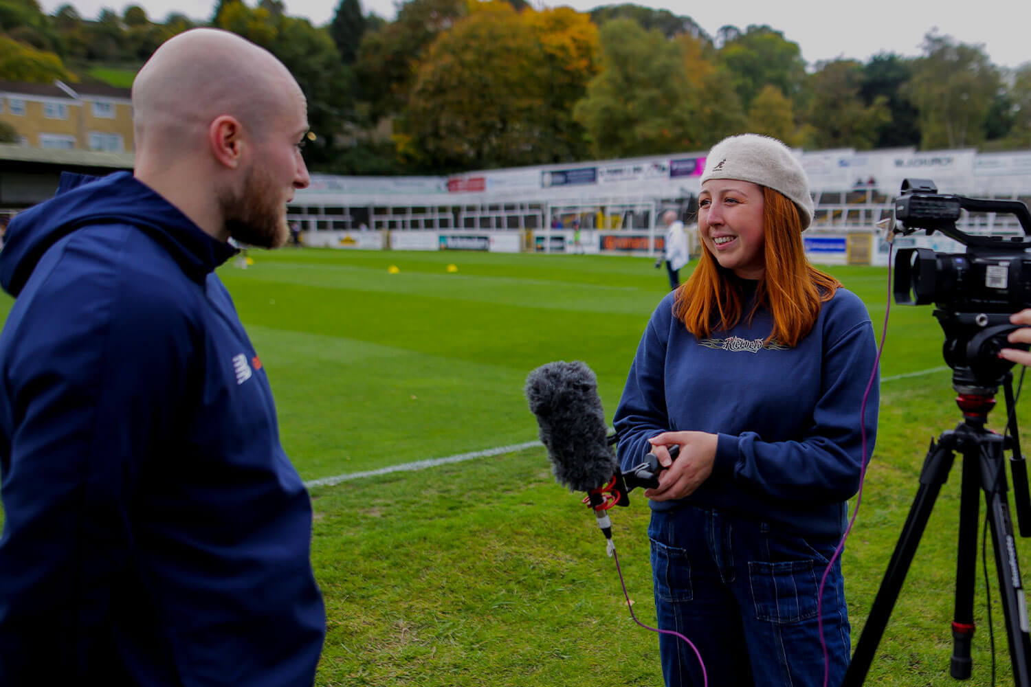 Student with mic talking with sports professional on a pitch