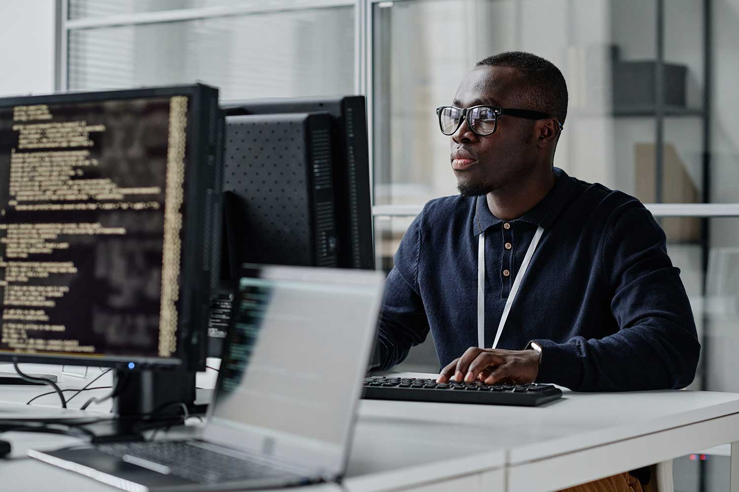 A student wearing a lanyard works at a desktop PC
