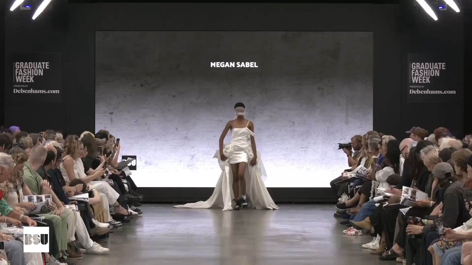 A person walks on a catwalk with the audience lining either side of the room
